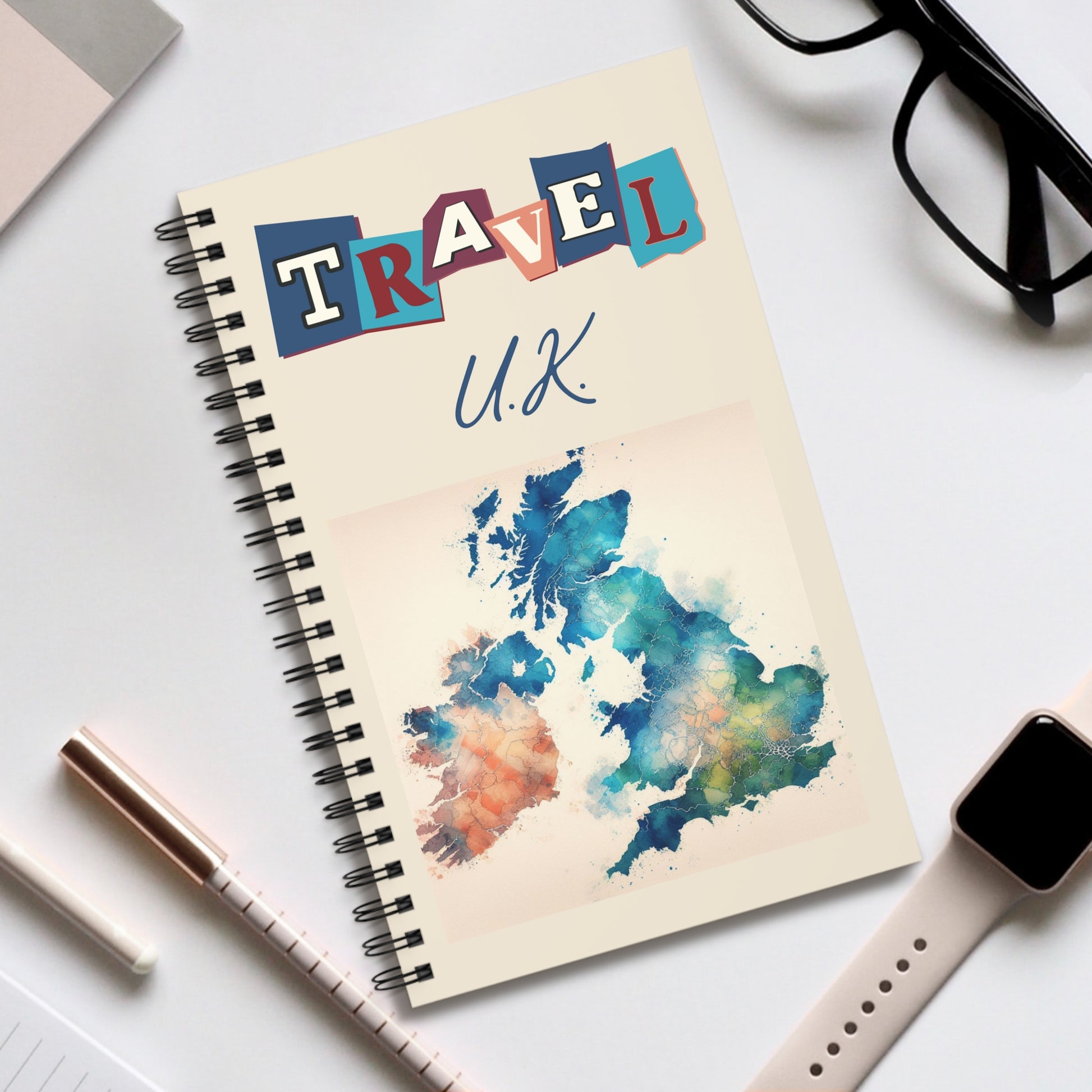 Prodigis spiral-bound UK-themed travel notebook features a vibrant watercolor map of the U.K. with TRAVEL in bold letters on the cover, surrounded by a pen, glasses, and smartwatch on a white surface—perfect for documenting your British cultural adventures. Choose your page design!.