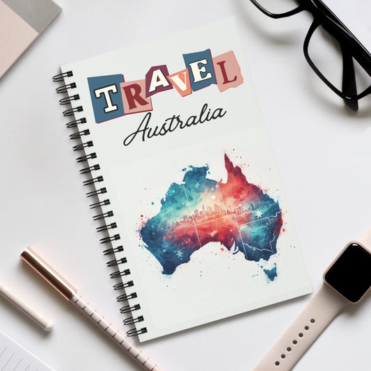 The Travel Australia spiral-bound notebook by Prodigi, featuring a colorful map and cityscape, rests on the desk. Nearby are glasses, a pen, and a smartwatch with a beige strap—ideal for jotting down adventures in this Australian travel journal with your choice of dot grid, lined or blank pages.