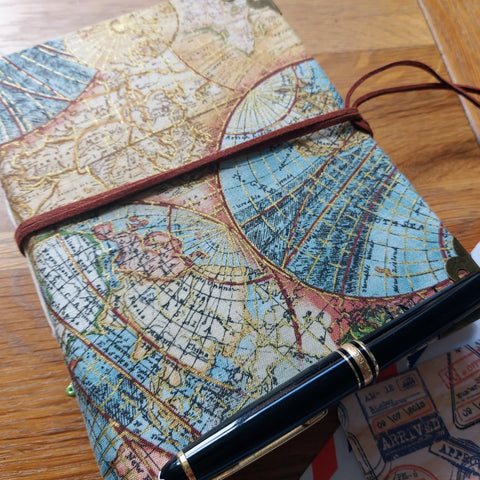 travel fabric hardback covered travel journal with vintage map images highlighted with gold.  Faux-suede lace to fasten, shown with MOnt Blanc pen