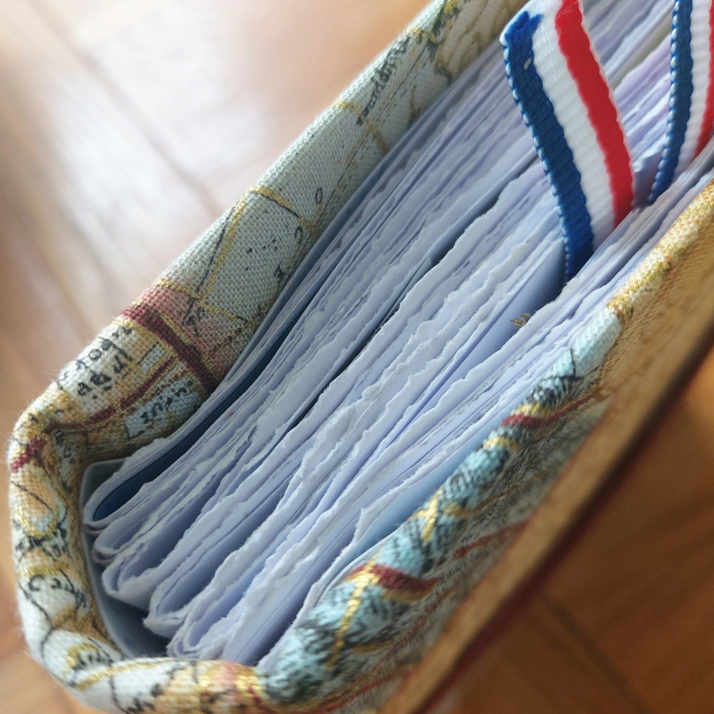 travel fabric hardback covered travel journal with vintage map images highlighted with gold. Top view shows hand torn edges to the paper to create texture and character. Ribbon trimmed paperclip bookmark