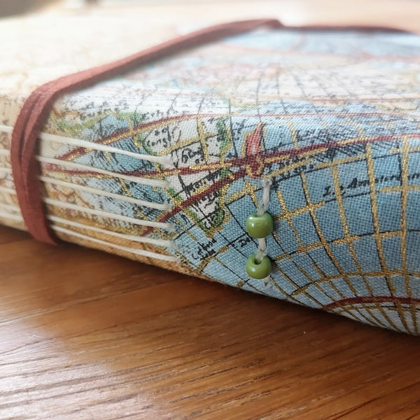 travel fabric hardback covered travel journal with vintage map images highlighted with gold.  Faux-suede lace to fasten, soft spine trimmed with small glass beads