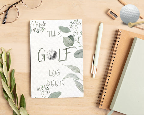 LAdies Golf log book with leaf design and a golf ball substituting the letter O, sitting on a dest with 2 other notebooks, pen, glasses, golf ball and tee