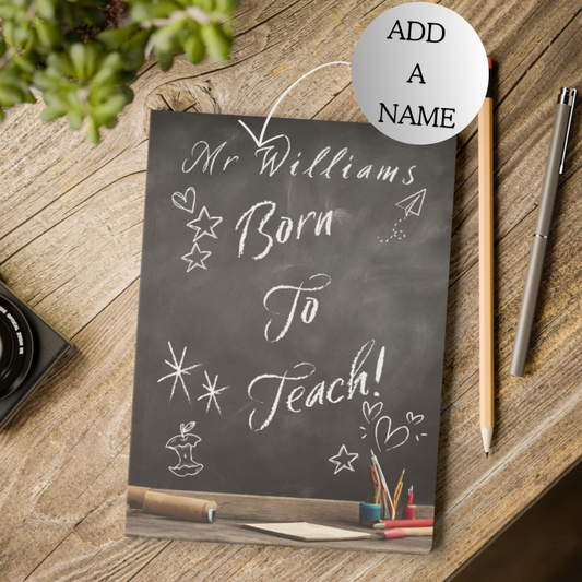 Personalized chalkboard notebook with 'Mr Williams Born To Teach!' on a wooden surface with stationery items.