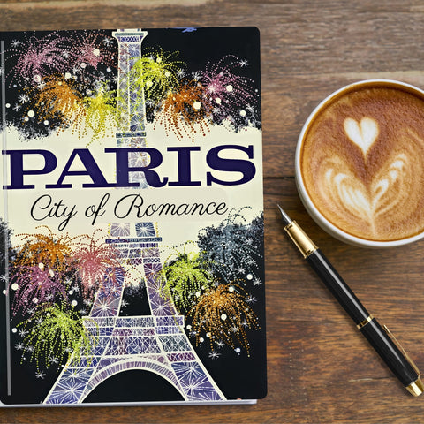 Paris Travel Journal with Eiffel tower surrounded by colourful fireworks .  Pen and coffee sit at the side of the travel journal
