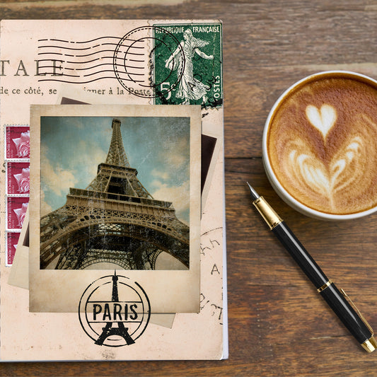 vintage photo of the eiffel tower over french postal themed elements make up the front cover of a travel journal for paris.  Cup of coffee and pen to the side