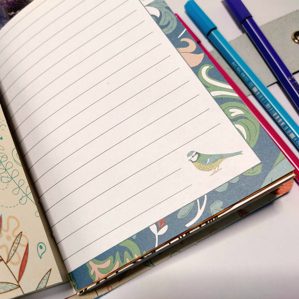 an open mixed paper travel journal with a lined page decorated around the edge and a blue tit bird in the corner