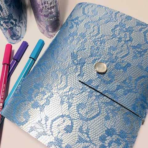 bright blue leather journal embossed with a lace design.  3 pens and 3 further journals to the left