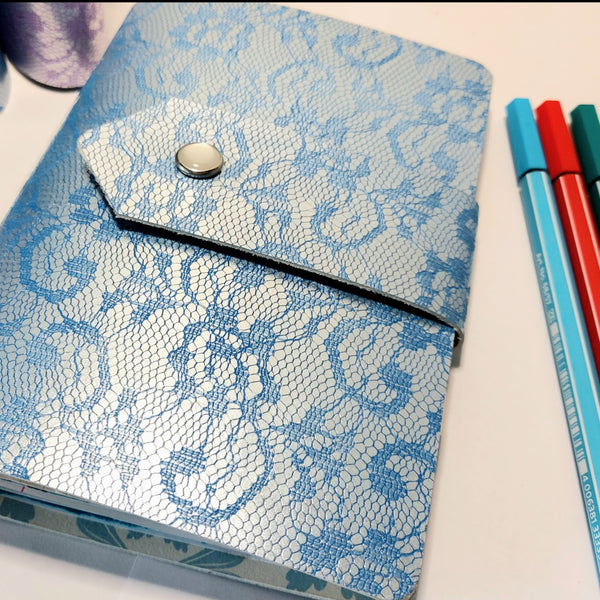 Blue leather journal embossed with a lace design.  Strap fastening with pearly stud fastener, 3 pens, blue, red and green