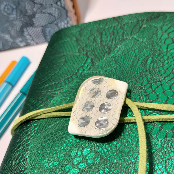 close up of vintage button and suede lace wrapping around a rich green embossed leather journal notebook