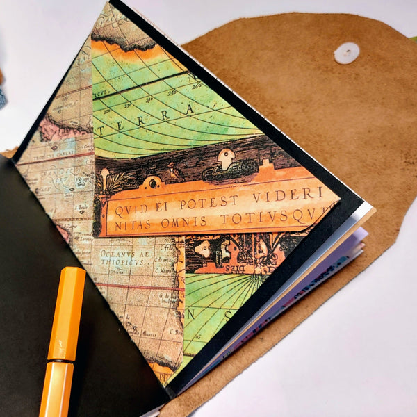 an open journal notebook containing mixed paper pages and housing a vintage map envelope stitched into the centre