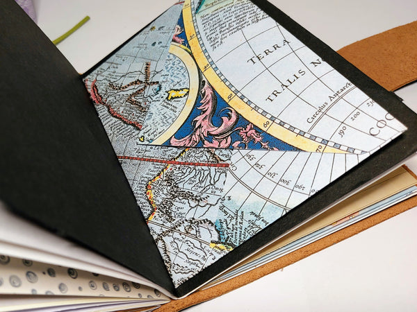 open pages of mixed paper journal notebook with vintage map printed envelope sewn into the centre