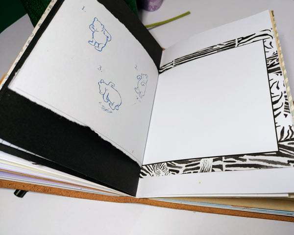 open notebook showing a variety of mixed paper pages.  solid black page and half page showing winnie the pooh sketch