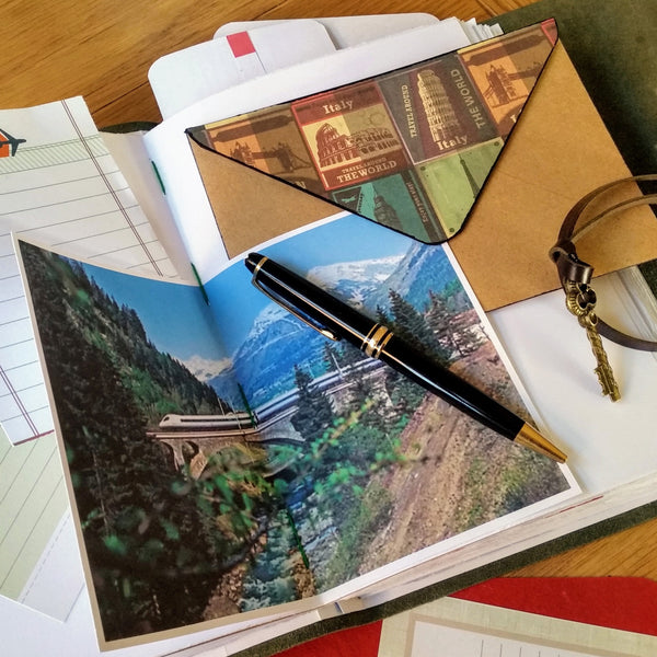 Open Pages in travel journal showing custom envelope, pen and high speed rail bridge with Italian alps mountain view