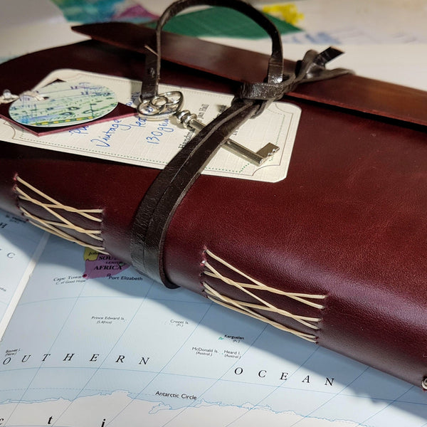 Large Burgundy Leather Travel journal with key trim sat on worl map