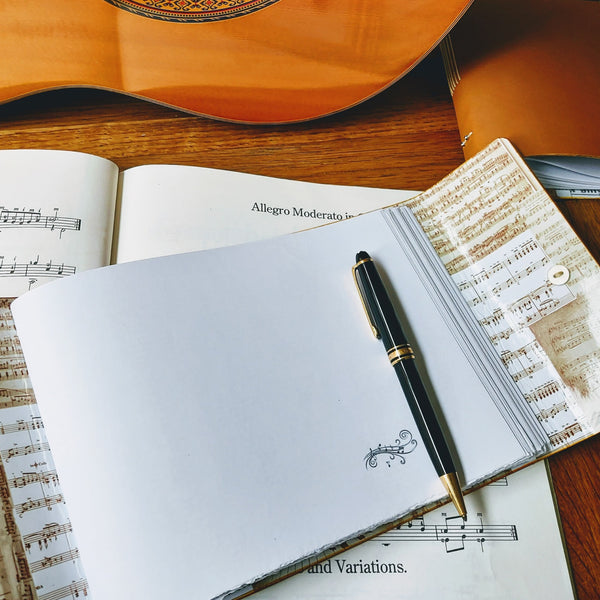 open music composintion book with blank forst page ready for inscription, guitar in background and mont blanc pen
