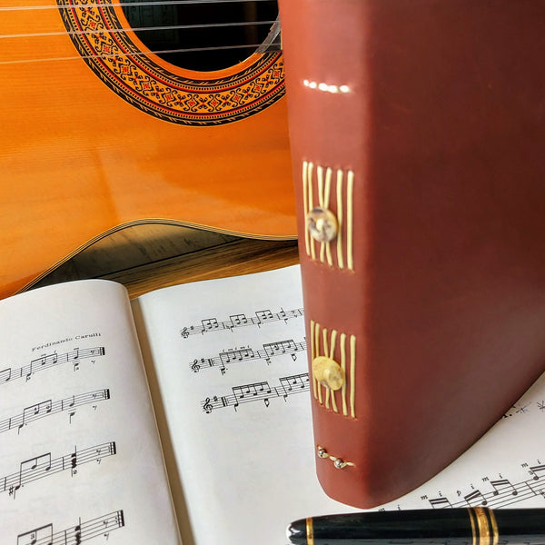Bespoke Bindery leather music journal with button trim on spine by guitar and pen